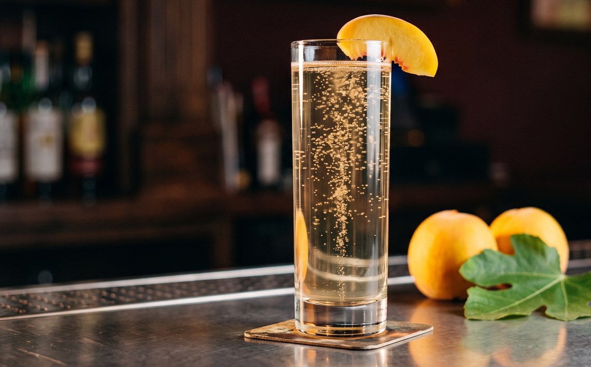 Peach and fig leaf highball served without ice in a chilled glass, fine bubbles, peach crescent on the rim